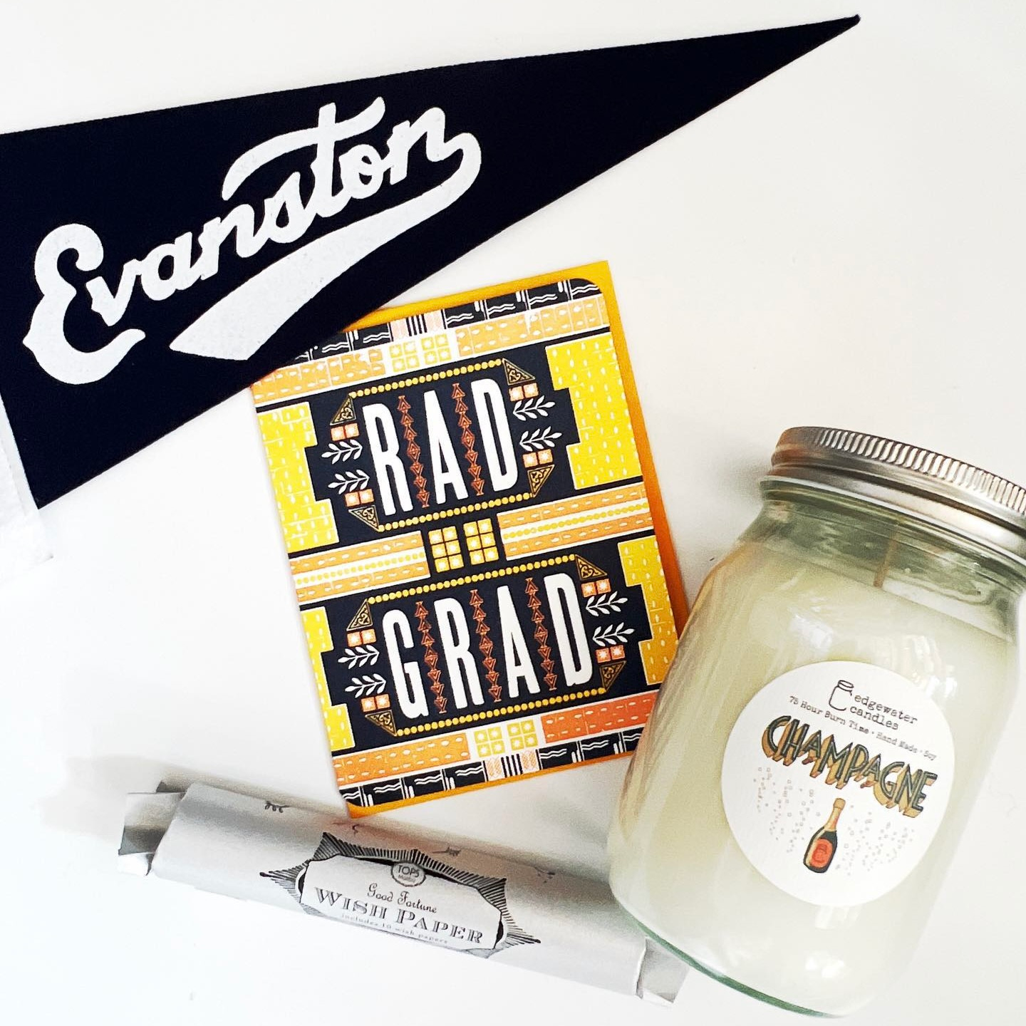 Graduation cards and gifts available at Stumble & Relish. Items shown: Rad Grad Greeting Card, Champagne Soy Wax Candle, Evanston Pennant, and Wish Paper.